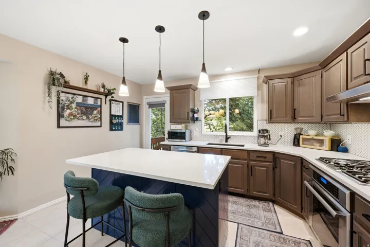 Spacious kitchen featuring a central island with white countertop, dark blue paneling, and three pendant lights