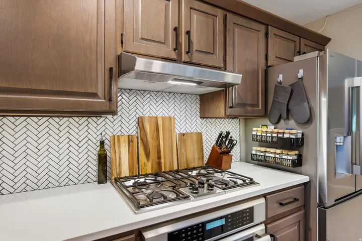 Gourmet kitchen featuring brown cabinetry, white herringbone tile backsplash, and white countertops