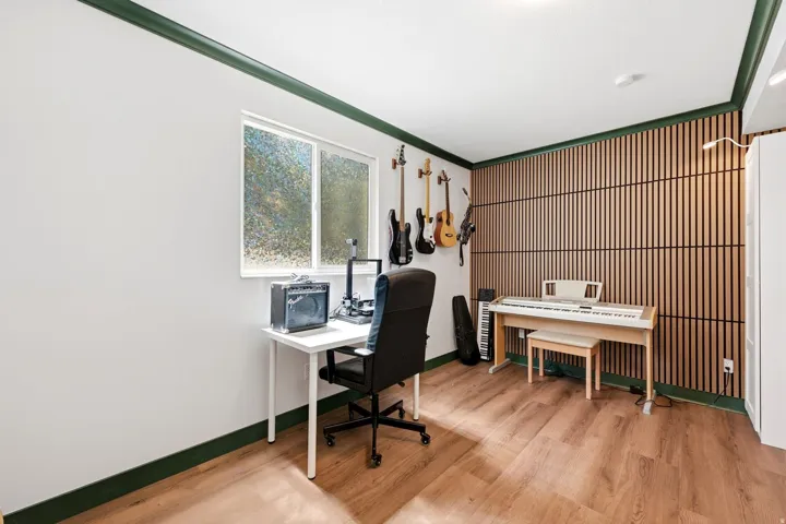 Versatile room featuring wood-finish flooring, a contemporary accent wall with vertical wood slats, and a white-framed window