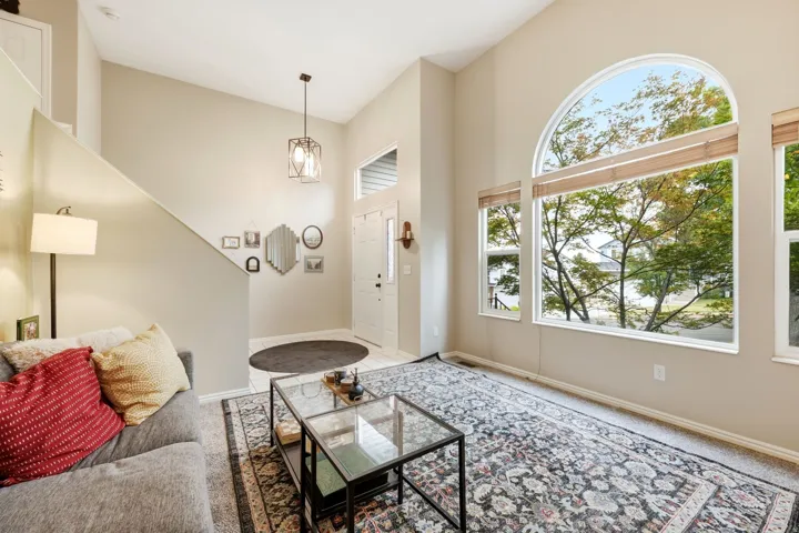 Living area featuring vaulted ceilings, a large arched window, multiple floor-to-ceiling windows, and carpet flooring