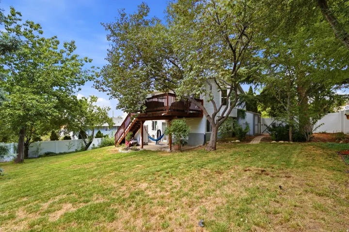 Expansive backyard featuring a sloped lawn, mature trees, a multi-level wood deck with stairs, a patio area, and a white privacy fence