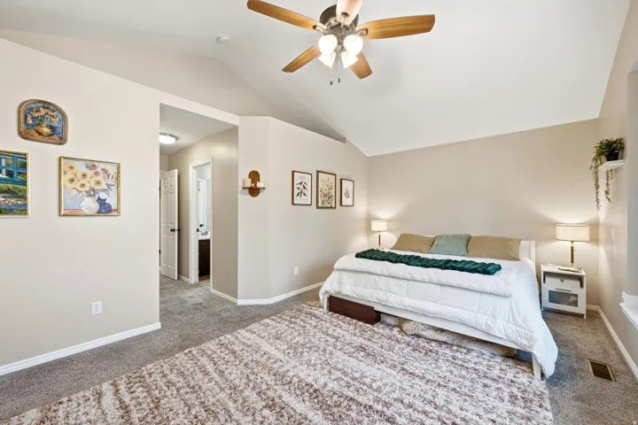 Carpeted sleeping area featuring a vaulted ceiling and a ceiling fan with integrated lighting