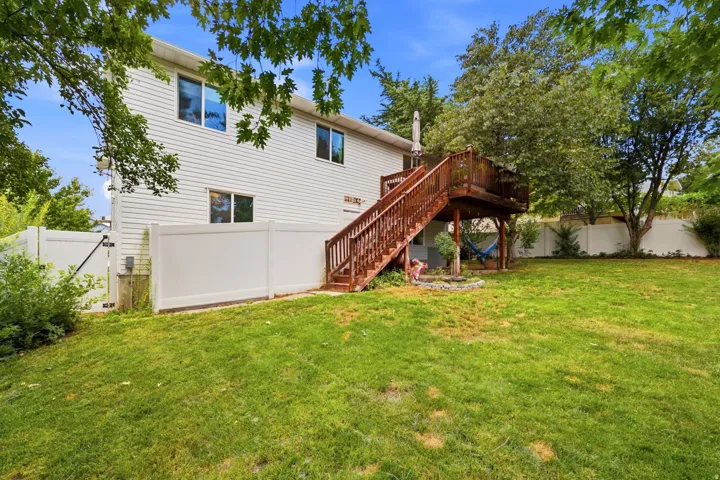 Spacious backyard featuring a large wooden deck with stairs, white vinyl fencing, and a manicured lawn