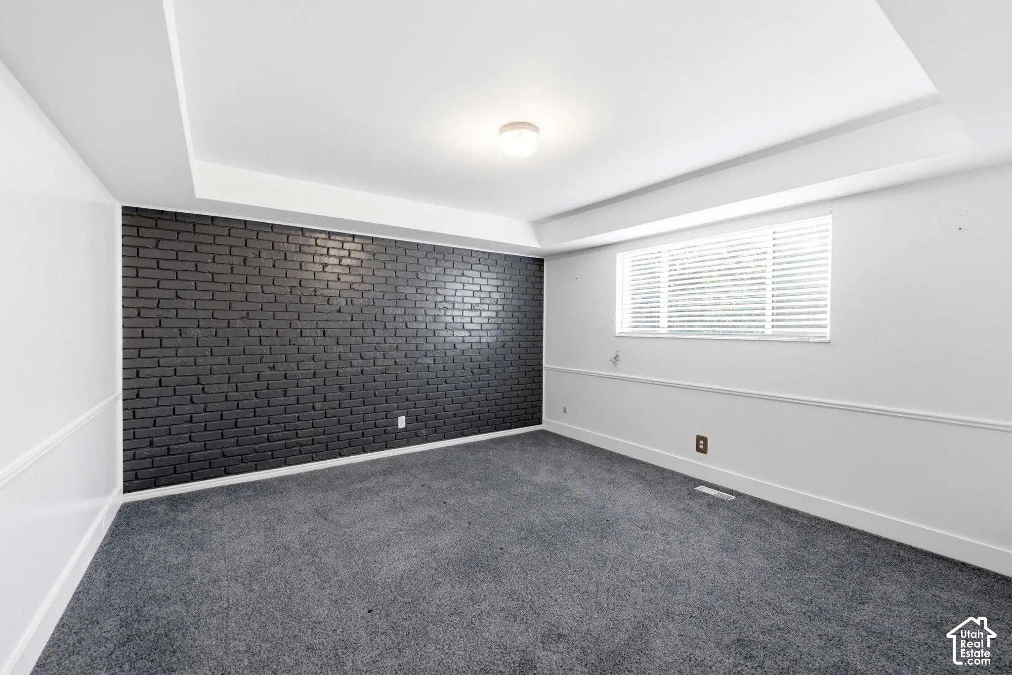 Large bedroom with fresh new carpet, natural light, and brick accent wall.