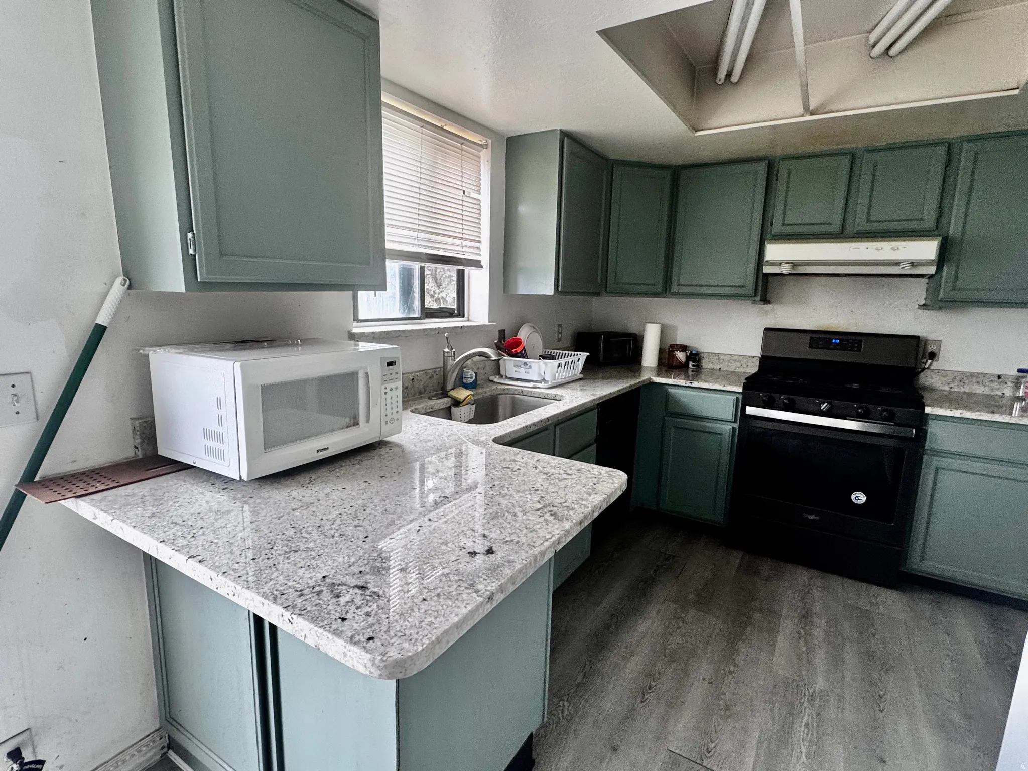 Kitchen featuring light teal cabinetry, granite-finish countertops, stainless steel sink, and wood-finish flooring