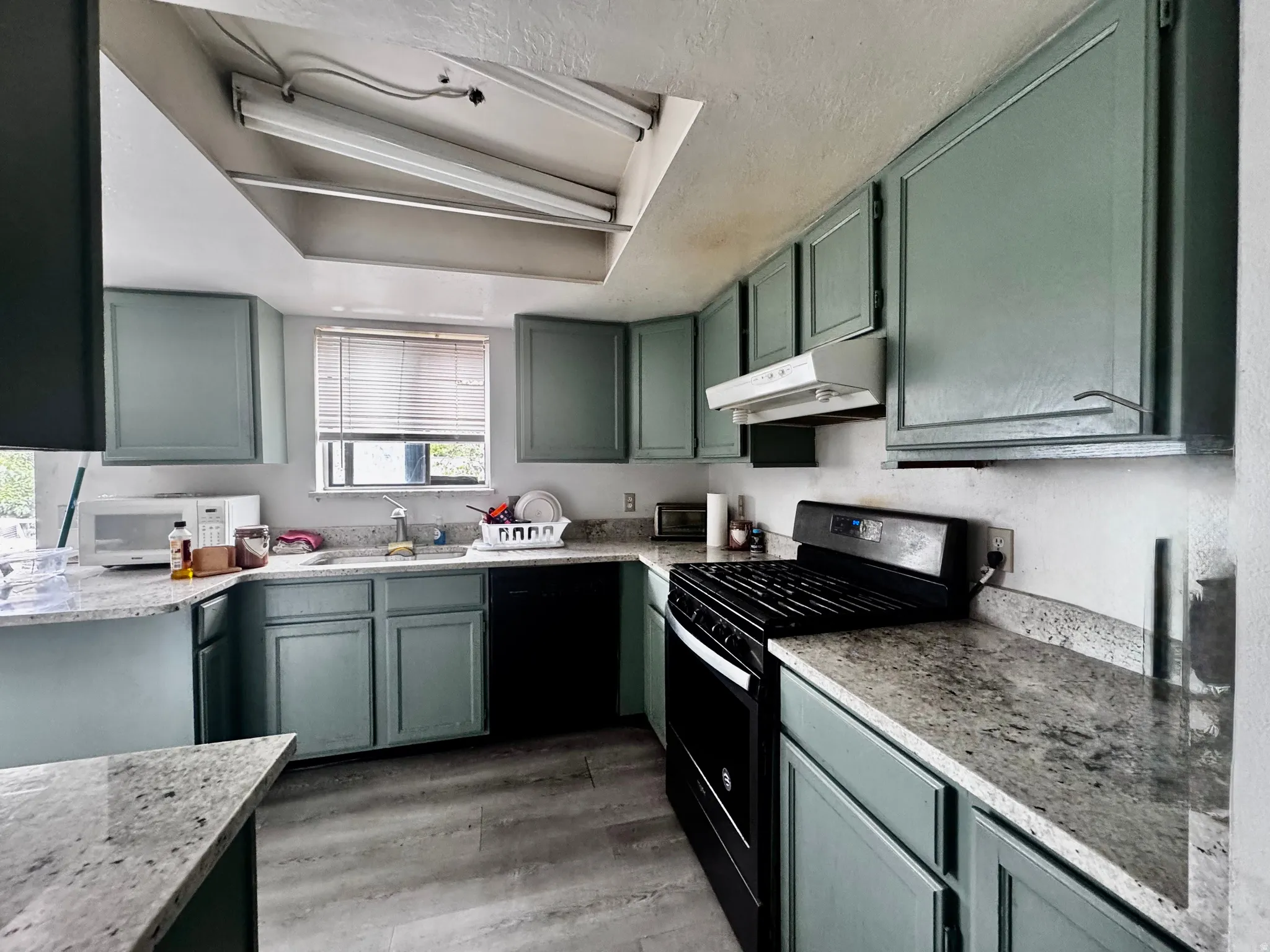 Kitchen featuring wood-finish flooring, light-toned countertops, and a full suite of black appliances