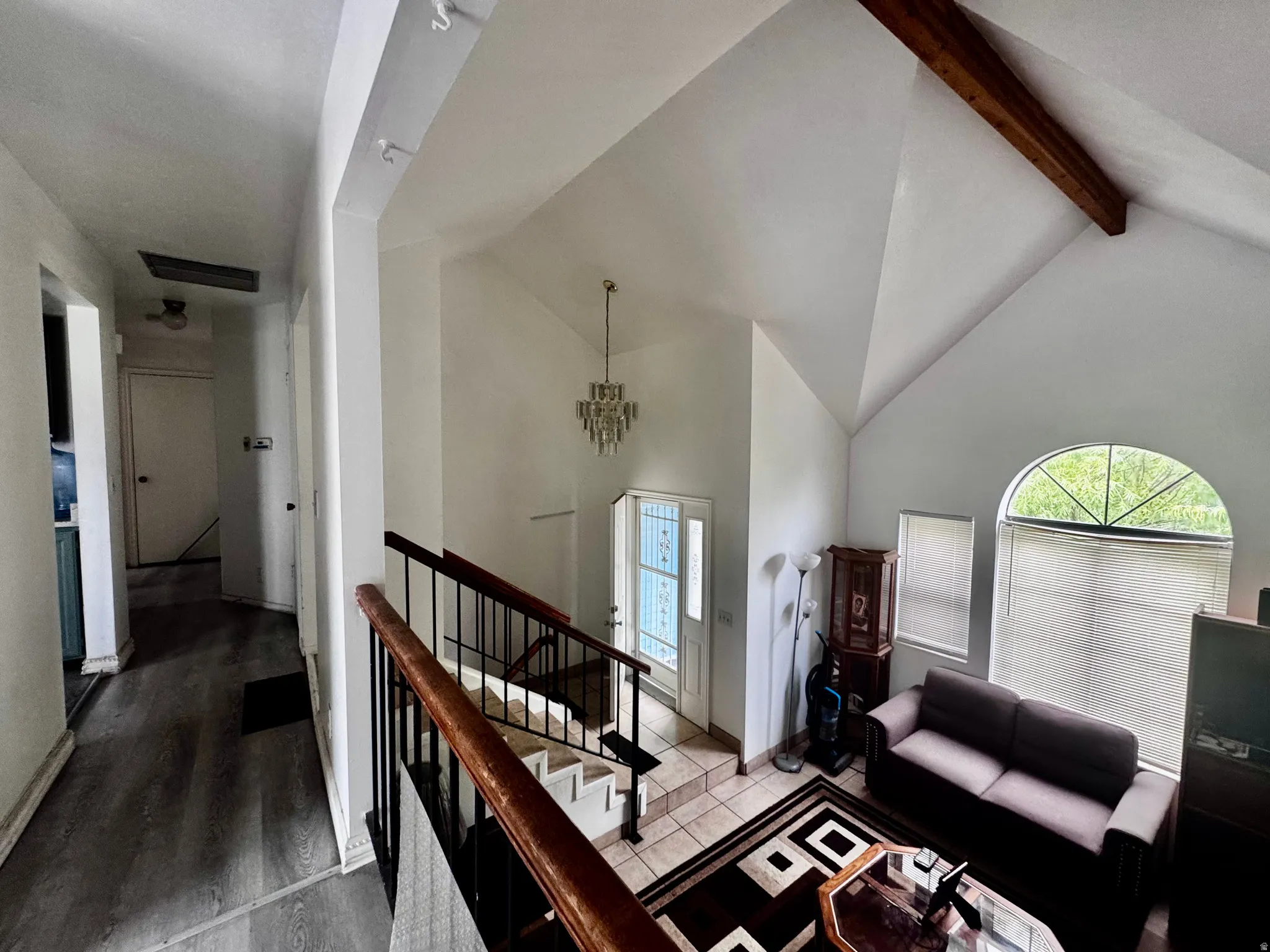 Entry foyer featuring a vaulted ceiling with exposed wood beam, a crystal chandelier, and tiled flooring