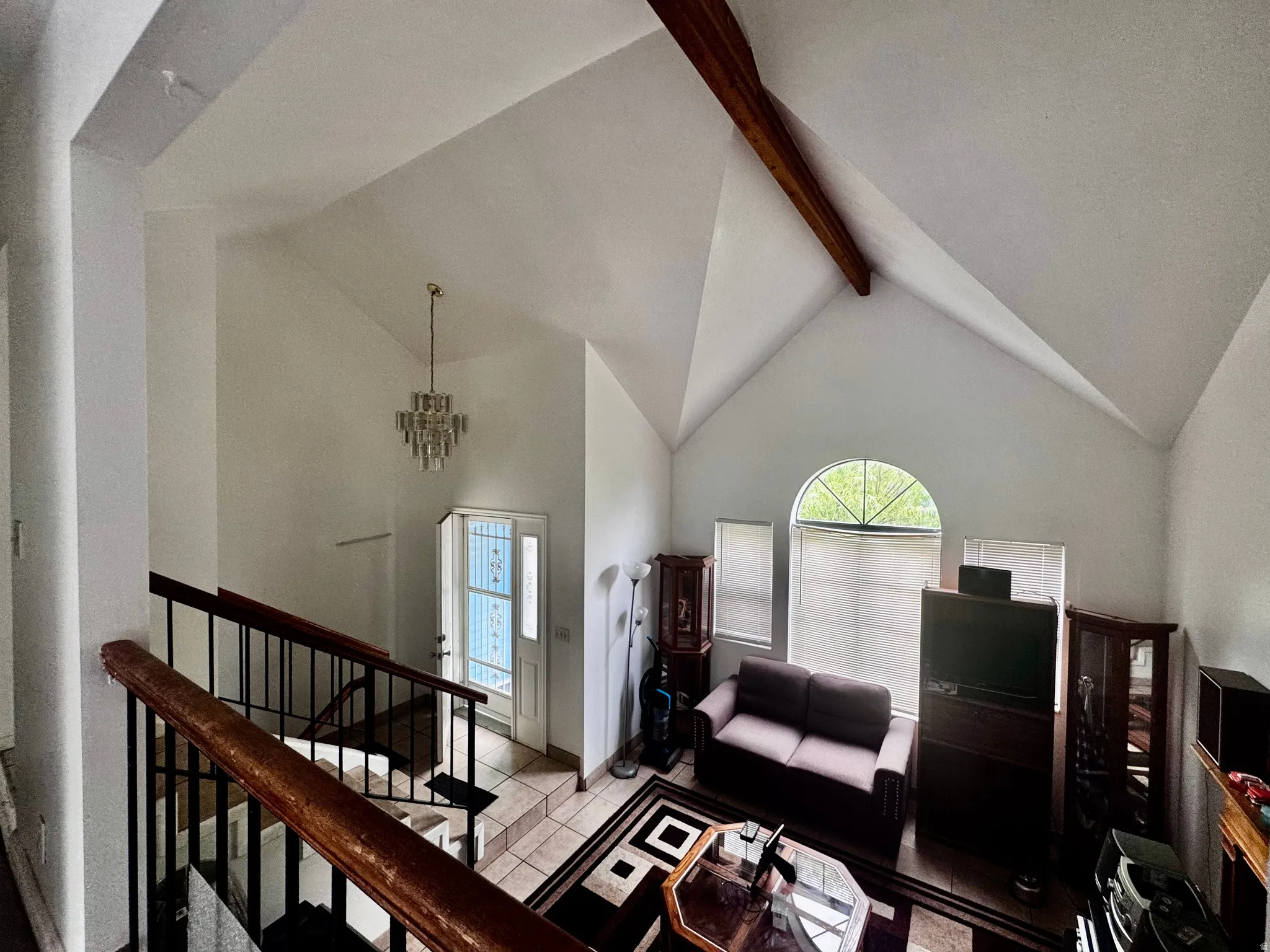 Vaulted ceiling space featuring a crystal chandelier, exposed wood beam, and a large arched window with two rectangular windows below