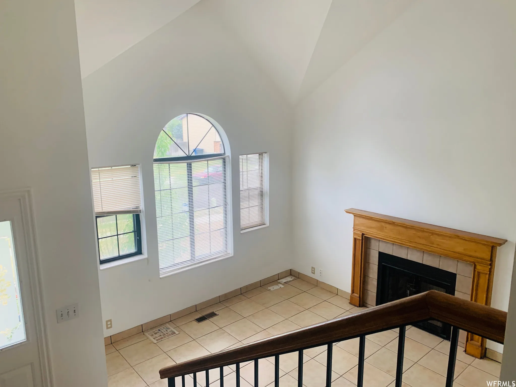 Vaulted ceilings accent a living space featuring a fireplace with a wood mantle and tile surround, and tile flooring