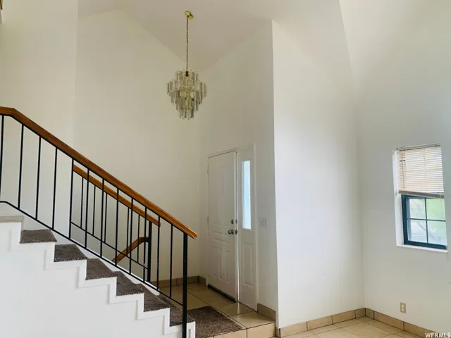 Entryway featuring a crystal-style chandelier, vaulted ceilings, and a staircase with a wood-finish handrail and wrought iron balusters