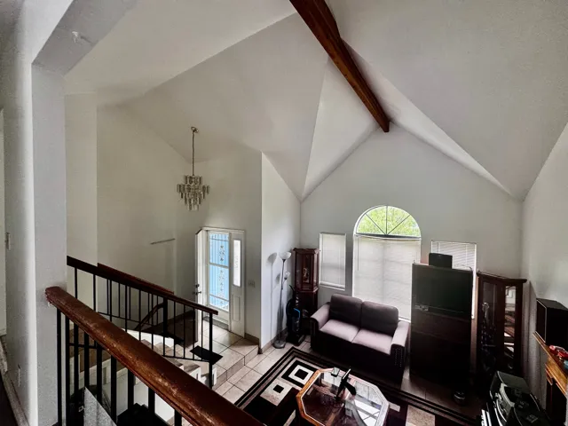 Vaulted ceiling space featuring a crystal chandelier, exposed wood beam, and a large arched window with two rectangular windows below