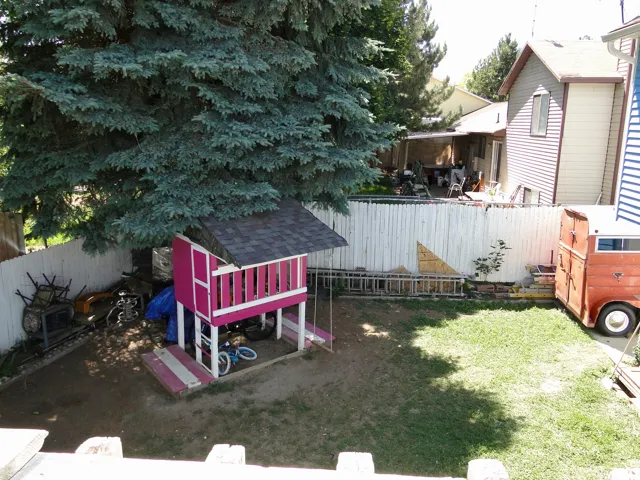 Expansive rear yard featuring a partial grass area, a mature evergreen tree, and a white picket fence