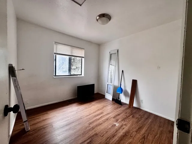 Room featuring wood-finish flooring, white walls, and a window with blinds