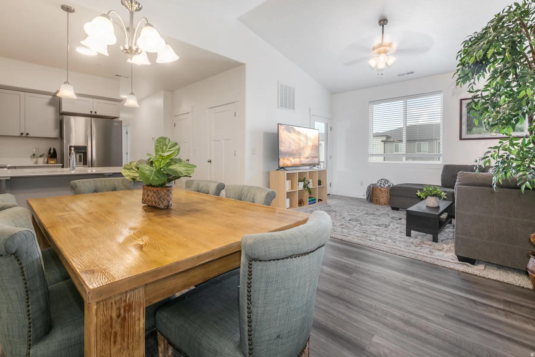 Open-concept living space featuring wood-finish flooring, vaulted ceilings, and a kitchen with stainless steel appliances, light gray cabinetry, and a peninsula with countertop seating