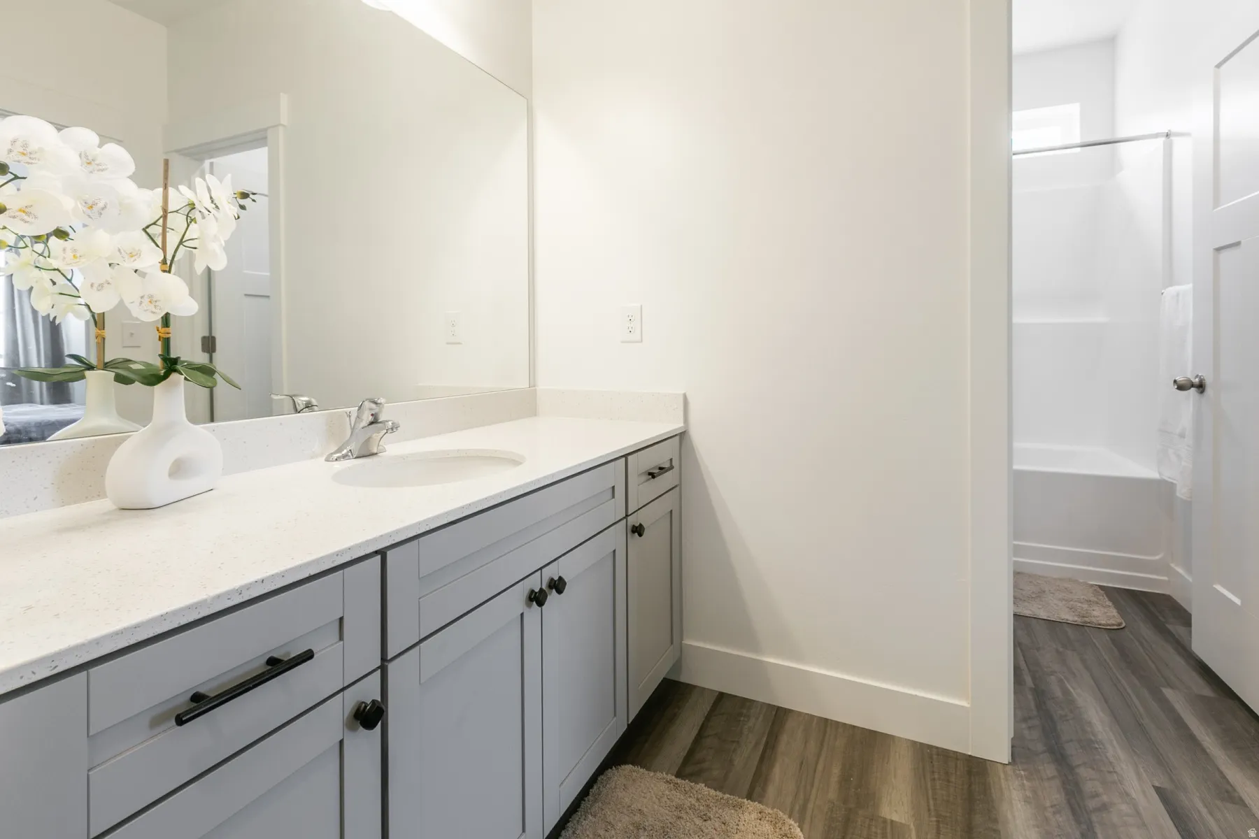 Bathroom featuring a white countertop with integrated sink, gray cabinetry with black hardware, wood-finish flooring, and a white tub/shower combination