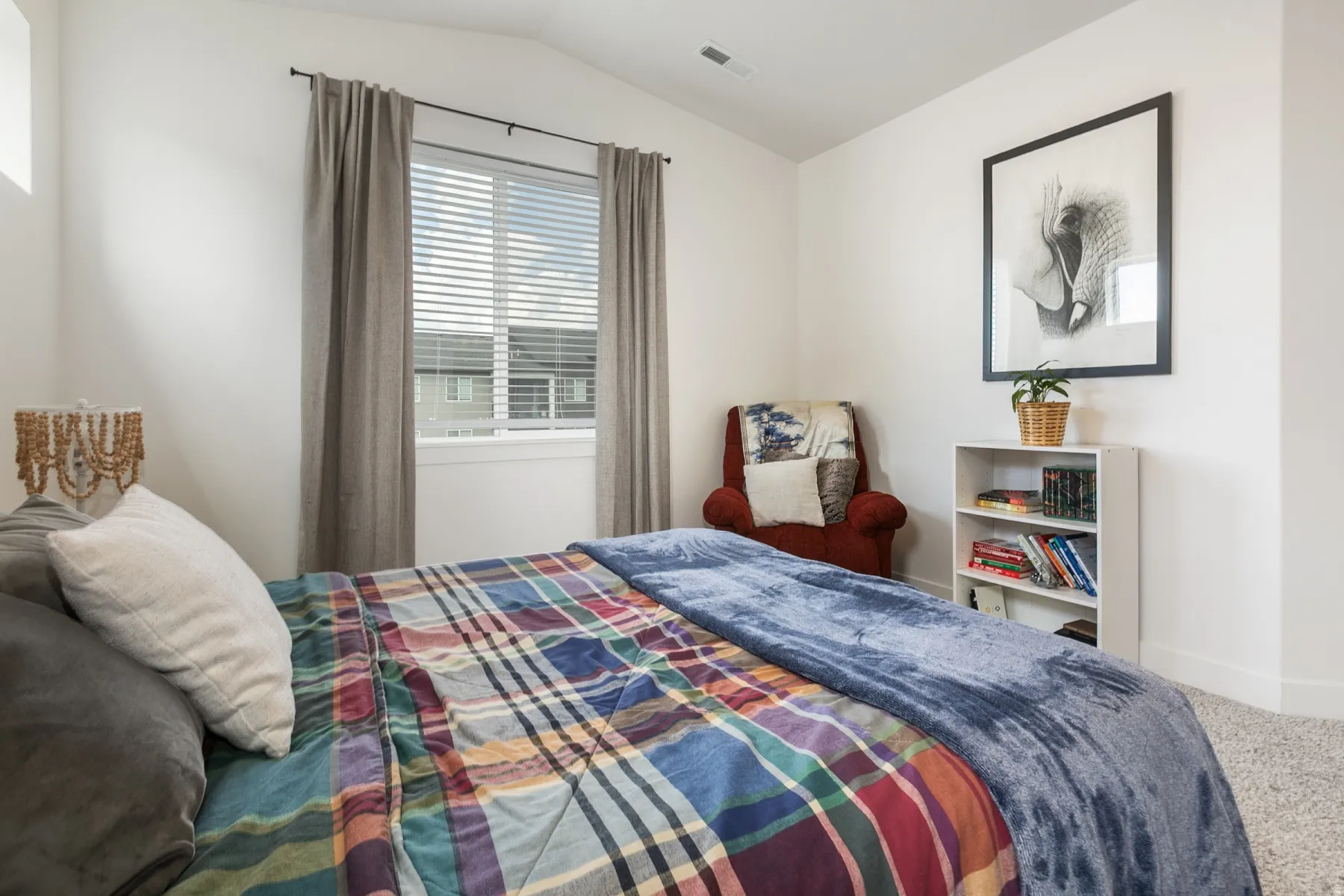 Bedroom featuring a window with blinds and drapes, white walls, and light-colored carpeting