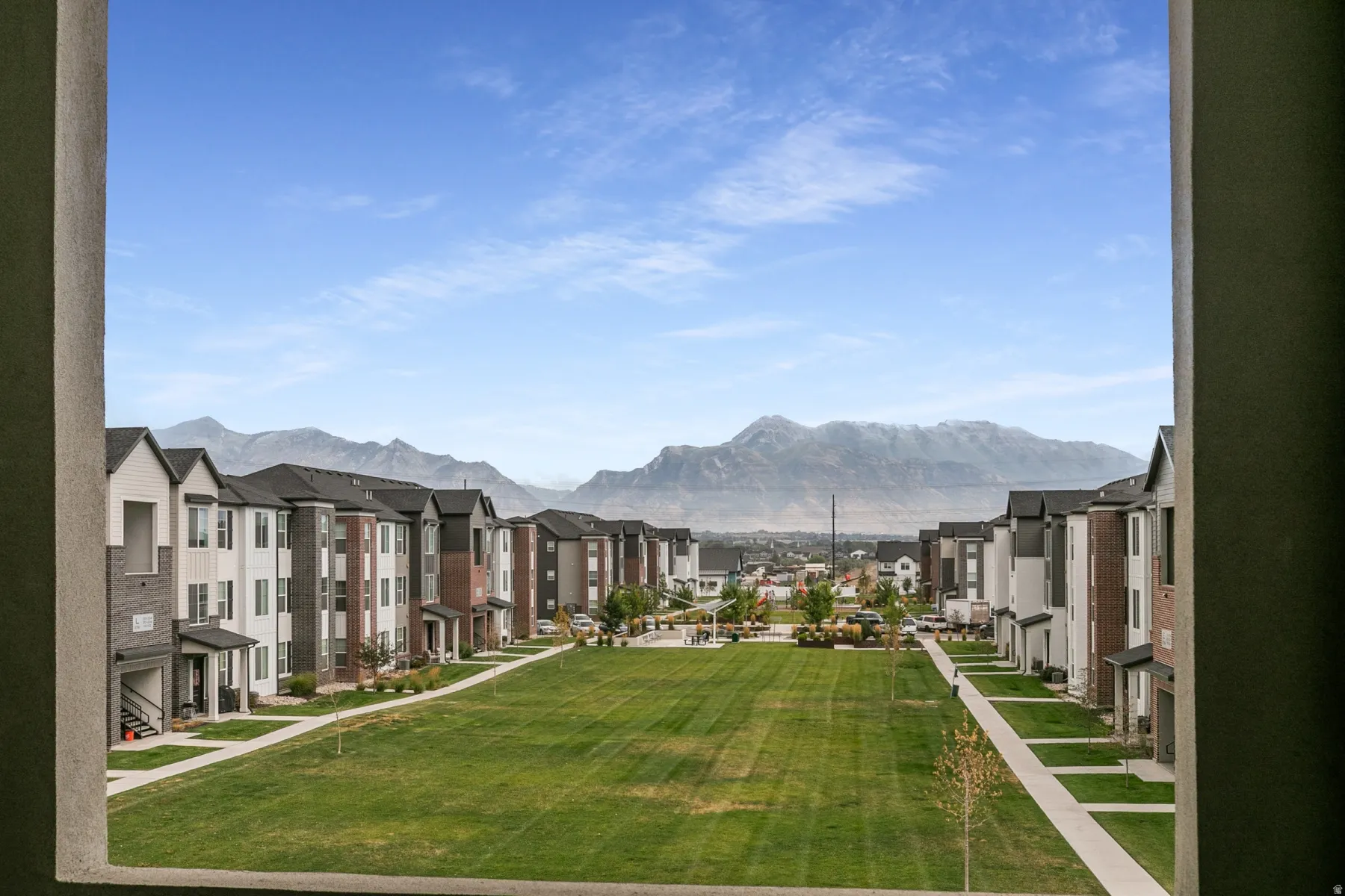 Expansive green space bordered by multi-story residential buildings featuring varied siding, pitched roofs, and mountain scenery