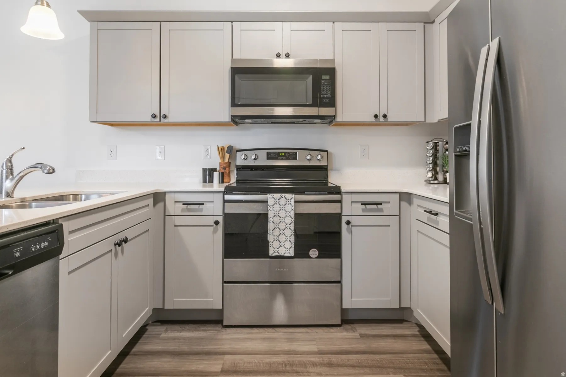 Modern kitchen featuring light gray shaker-style cabinetry, stainless steel appliances, white countertops, and wood-finish flooring