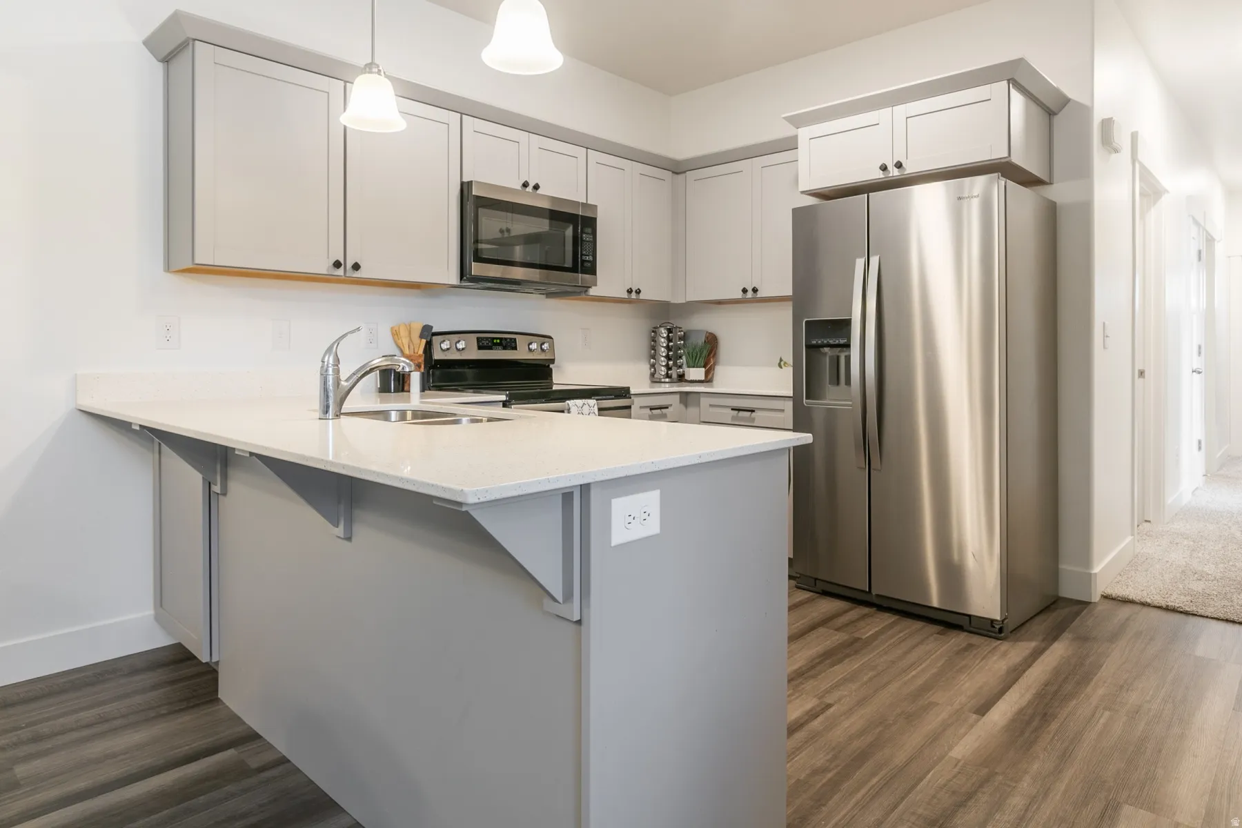 Contemporary kitchen featuring light gray cabinetry, stainless steel appliances, a center island with a double basin sink, light-toned countertops, and wood-finish flooring