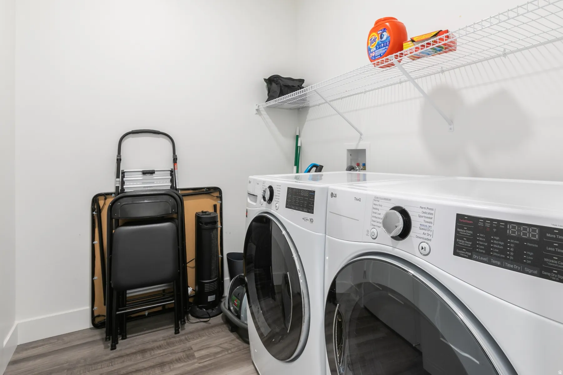 Dedicated laundry area featuring a front-load washer and dryer, white wire shelving, light wood-finish flooring, and crisp white walls