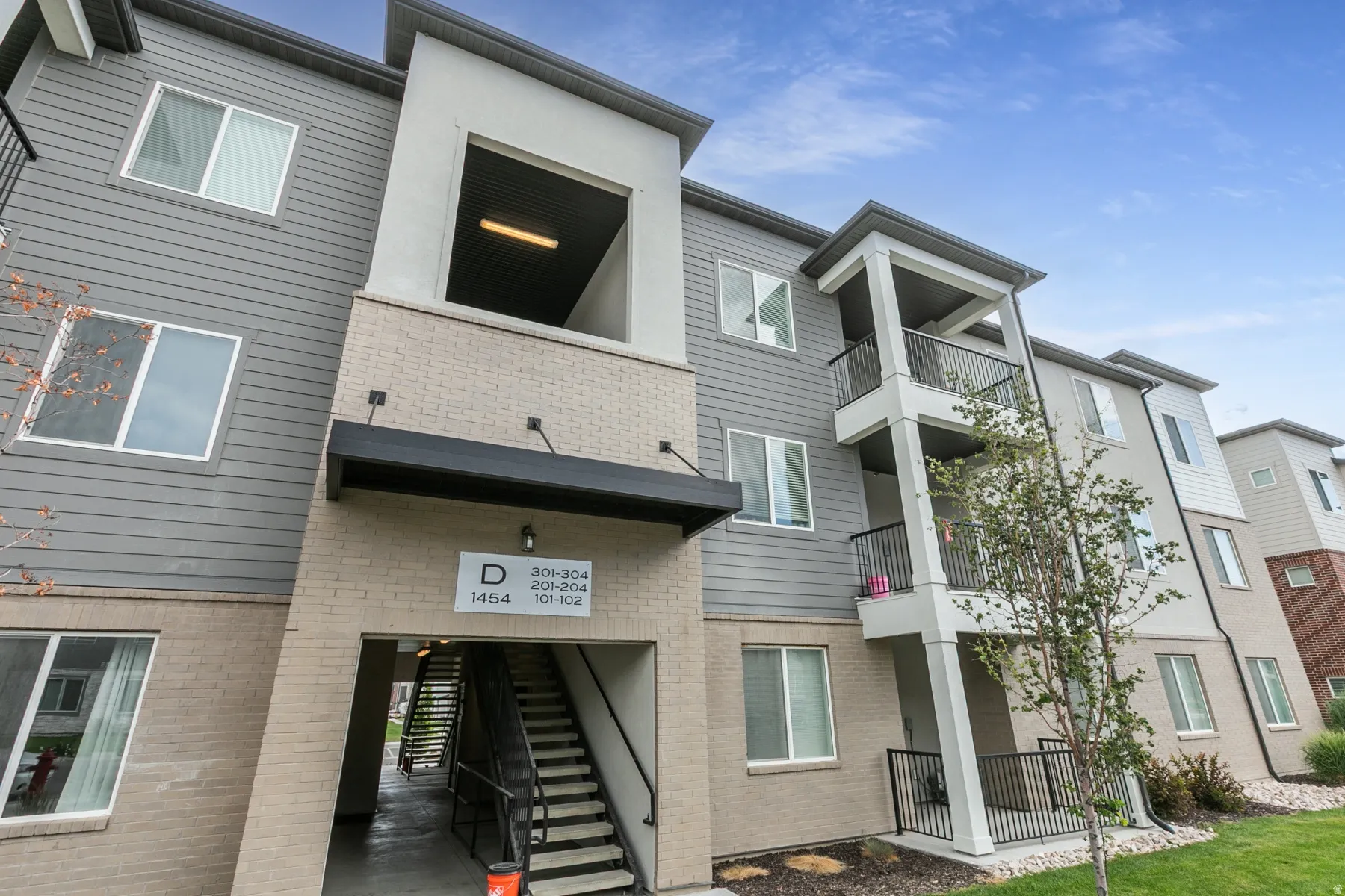 Multi-story building exterior featuring gray siding and tan brick accents