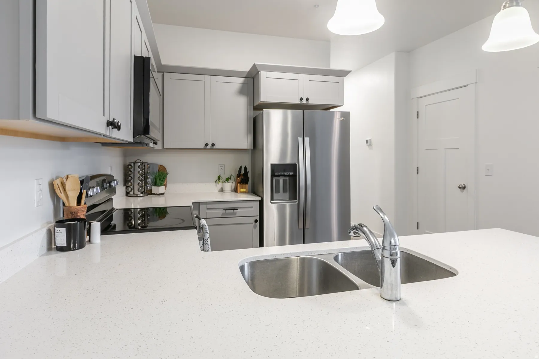 Kitchen featuring a double basin stainless steel sink with gooseneck faucet, light-toned countertops, gray cabinetry, stainless steel appliances, and an electric cooktop