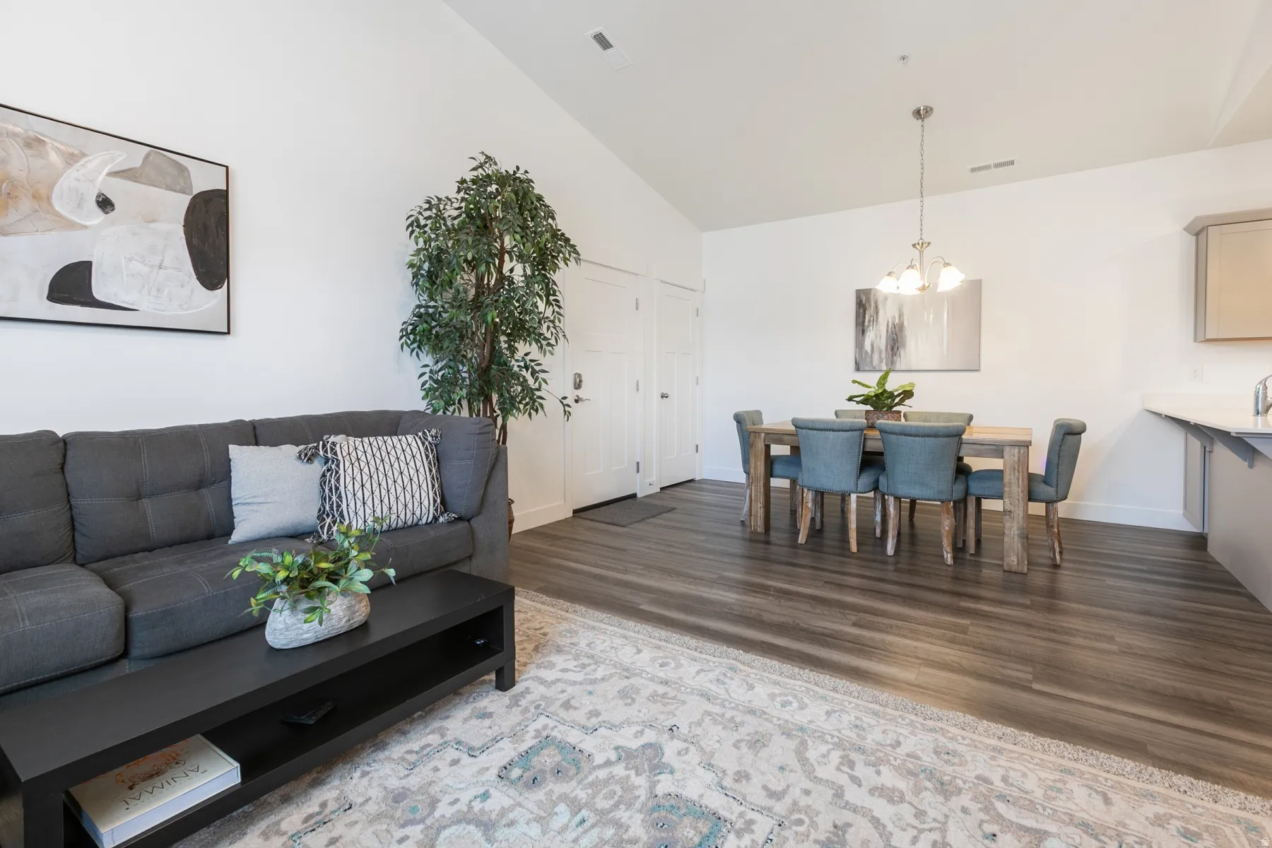 Open-concept living and dining area featuring vaulted ceilings, wood-finish flooring, and white walls
