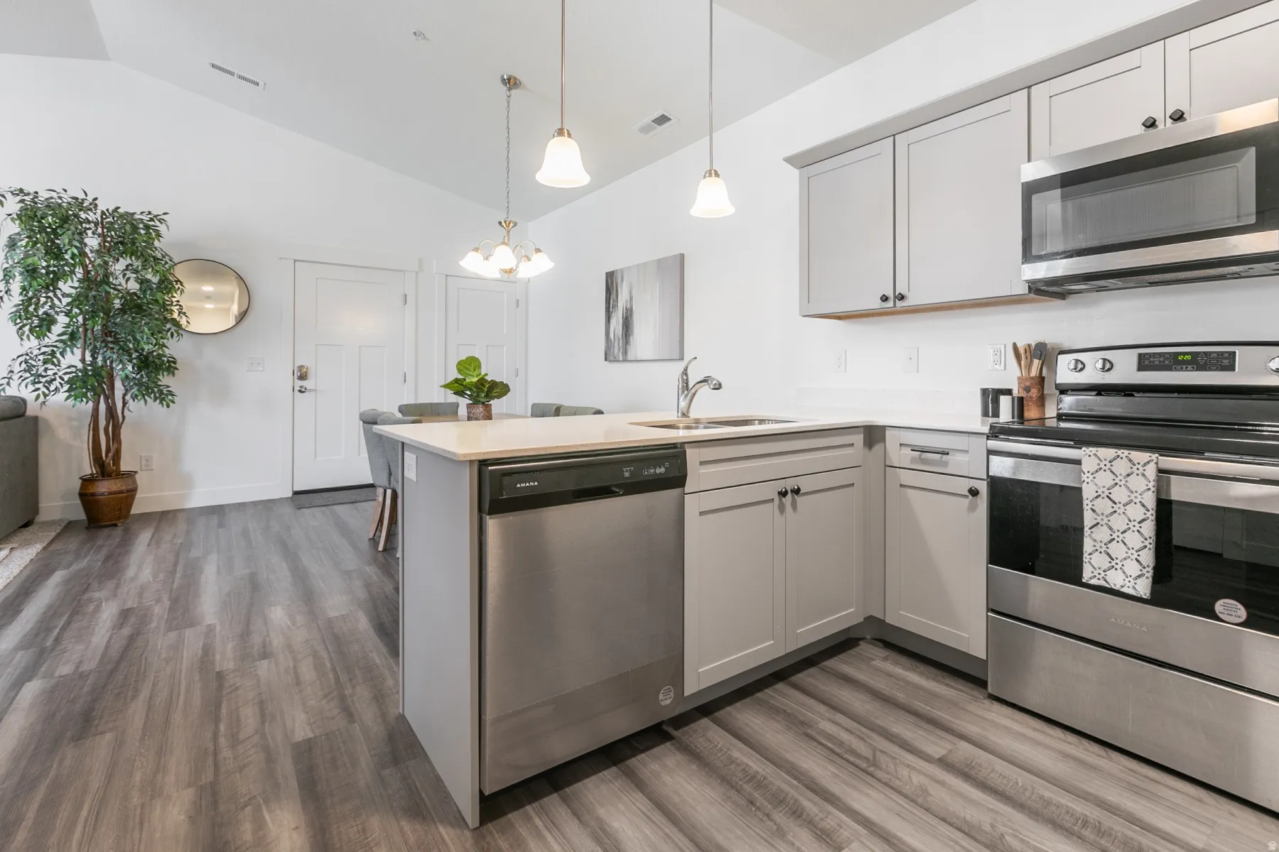 Modern kitchen featuring light gray cabinetry, stainless steel appliances, a white solid surface countertop, and wood-finish flooring