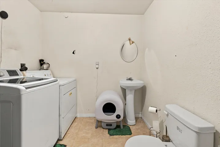 Pedestal sink with mirror, toilet, and light-colored flooring