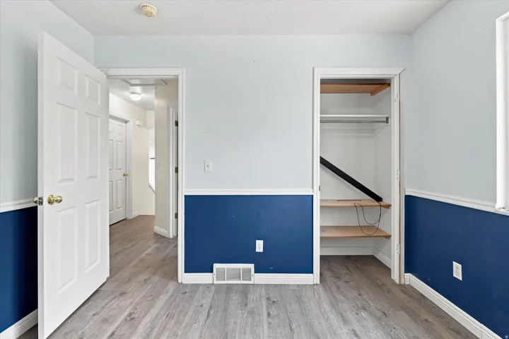 Interior space featuring wood-finish flooring, two-tone wall treatment, and a built-in closet with shelving and hanging rod