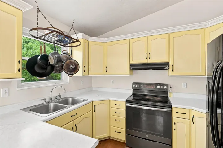 Kitchen featuring light yellow cabinetry with crown molding, double basin sink, white countertops, black electric range with coordinating range hood, and a black refrigerator
