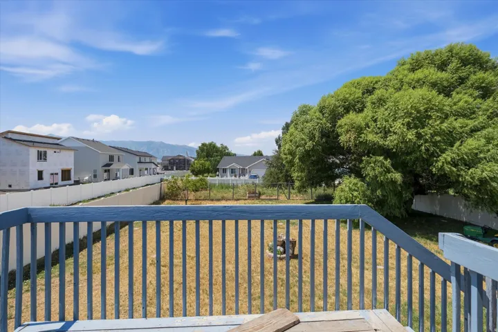Deck with blue-painted railing overlooking a yard with a large mature tree, perimeter fencing, and distant mountain range