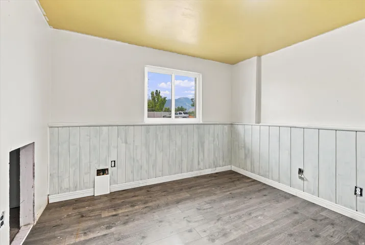Room featuring wood-finish flooring, white vertical plank wainscoting, and a window providing natural light