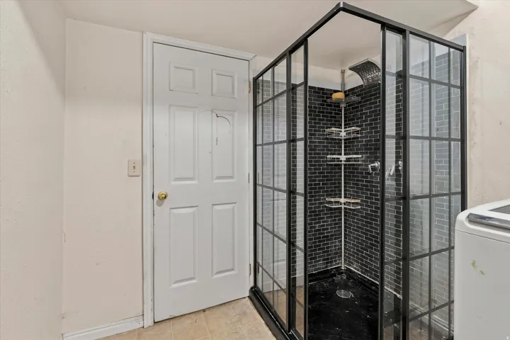 Walk-in shower with black-framed glass enclosure, black subway tile, and a built-in shelving unit