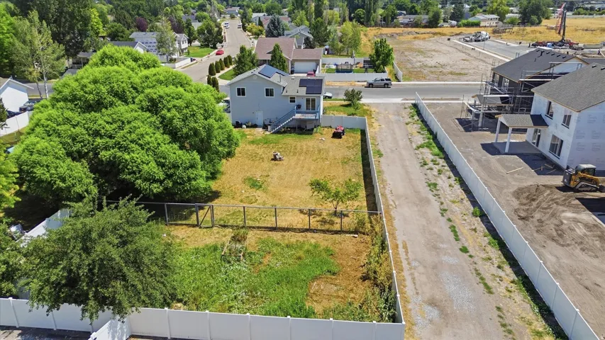 Expansive residential lot featuring a mature shade tree, partial fencing, and a gravel driveway