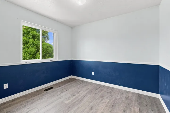 Room featuring wood-finish flooring, two-tone wall paint, white baseboards, and a white crown molding accent