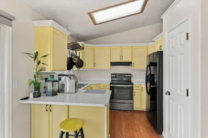 Kitchen featuring yellow cabinetry, light-toned countertops, and dark appliances