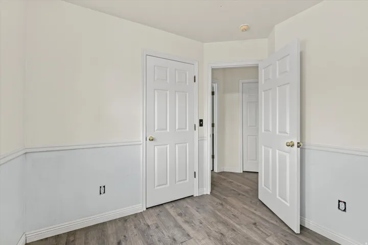 Interior space featuring wood-finish flooring, white panel doors with brass hardware, and two-tone walls with wainscoting