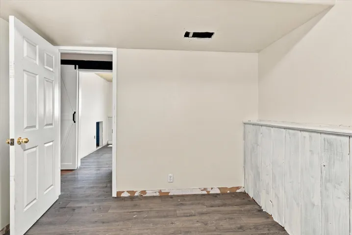 Interior space featuring wood-finish flooring, white paneled wainscoting, and a five-panel interior door with brass hardware