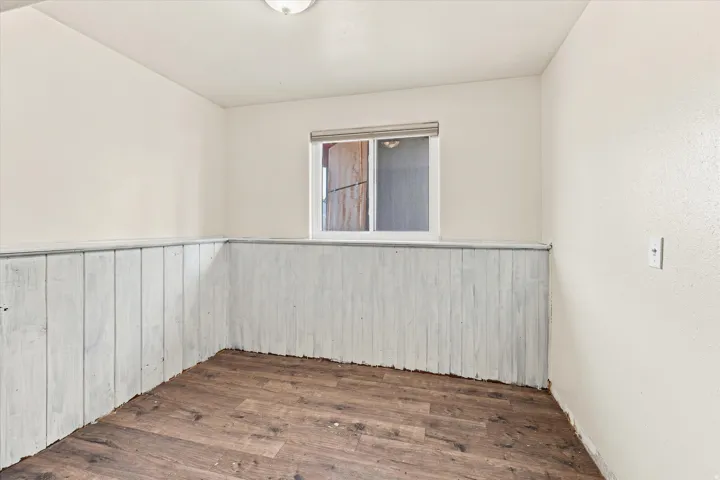Interior space featuring wood-finish flooring, white wall paneling, and a white framed window