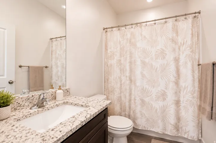 Bathroom featuring a dark wood-finish vanity, granite countertop with integrated sink, chrome faucet, and a wall-mounted mirror