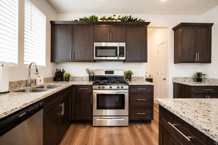 Well-appointed kitchen featuring dark wood-finish cabinetry, light-toned granite countertops, and stainless steel appliances