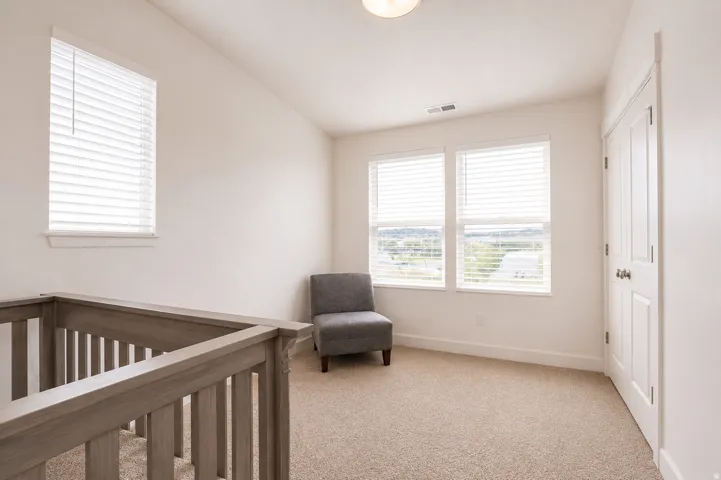 Carpeted loft area featuring a wood-finish railing, multiple windows with blinds, and a white paneled door