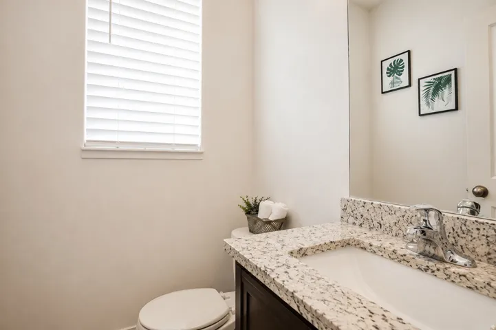 Window with blinds, white walls, built-in vanity with light-toned countertop, integrated sink, and chrome faucet
