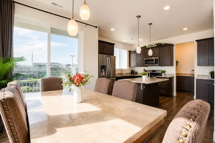 Open-concept kitchen and dining space featuring wood-finish flooring, dark wood cabinetry, a center island with pendant lighting, and stainless steel appliances