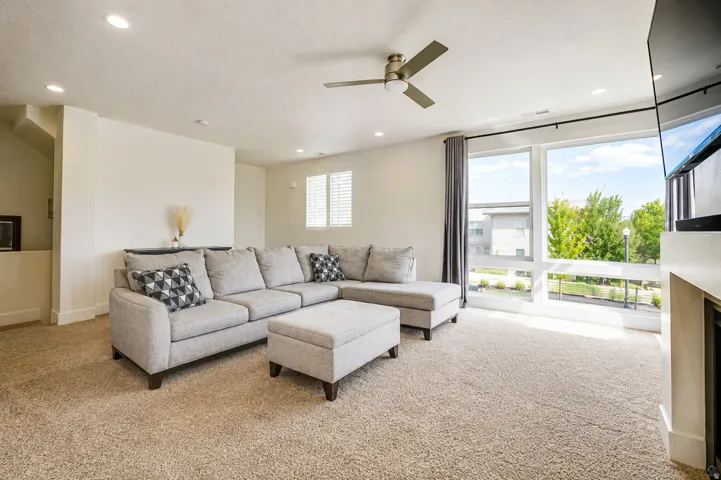 Recessed lighting, large picture windows, ceiling fan, built-in media console, and neutral carpeting