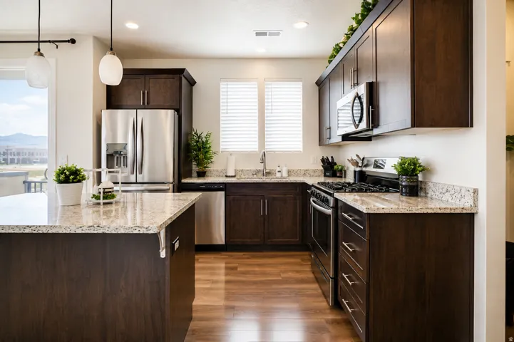 Kitchen featuring dark wood-finish cabinetry, stainless steel appliances, speckled stone countertops, a central island with pendant lighting, and wood-finish flooring