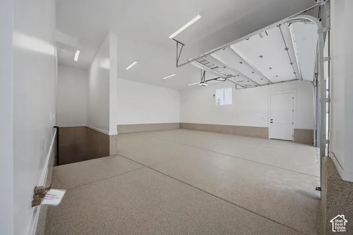 Expansive garage featuring a light-toned epoxy-coated floor, white painted walls, and overhead linear lighting fixtures