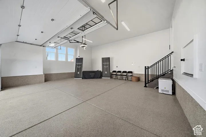 Spacious garage featuring a durable epoxy floor, a wall of windows, a black iron railing leading to an upper level, an overhead garage door with translucent panels, and bright overhead lighting
