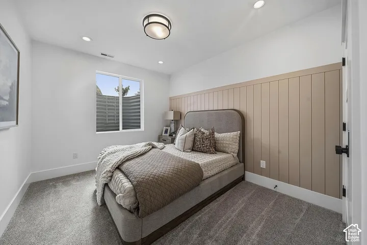 Bedroom with a neutral-toned accent wall featuring vertical paneling, recessed lighting, and a window with a window well